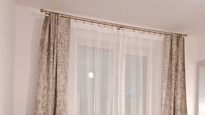 A black leather sofa with two cushions, a small round table, and a sheer curtain with a gold rod.