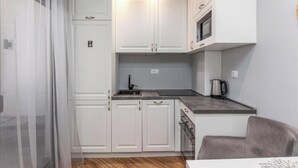 A compact kitchen with white cabinets, a microwave, a sink, and a coffee maker. - XIO Apartments | Stylish Comfort with Balconies & Full Kitchens (Bar)
