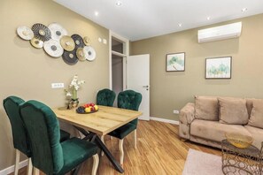 A dining area with a wooden table, green upholstered chairs, a fruit bowl, and wall art.