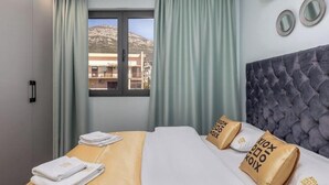 A hotel room with a bed, curtains, a window with a view, and a wall-mounted air conditioner. - XIO Apartments | Stylish Comfort with Balconies & Full Kitchens (Bar)