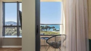 A room with a sliding glass door leading to a balcony with a view of the sea and hills. - XIO Apartments | Stylish Comfort with Balconies & Full Kitchens (Bar)
