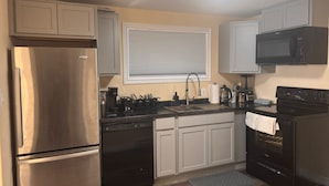 A kitchen with stainless steel appliances, white cabinets, a window with blinds, and a microwave.