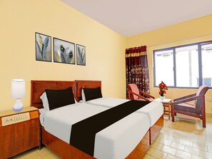 A hotel room with a double bed, a bedside table with a lamp, a chair, a small table with a vase, and a window with curtains. - Hotel O Gajuwaka Near Kurmanpalem (Visakhapatnam)