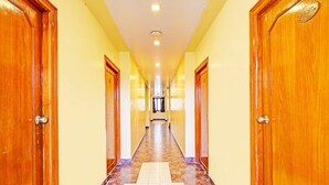 A long hallway with wooden doors on both sides, leading to a bright room at the end. - Hotel O Gajuwaka Near Kurmanpalem (Visakhapatnam)