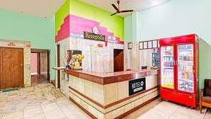 A hotel reception area with a reception desk, a clock, a 'No Smoking' sign, a 'Hotel S.B.T' sign, a 'Reception' sign, a 'Hotel O' sign, and a red beverage vending machine. - Hotel O Gajuwaka Near Kurmanpalem (Visakhapatnam)