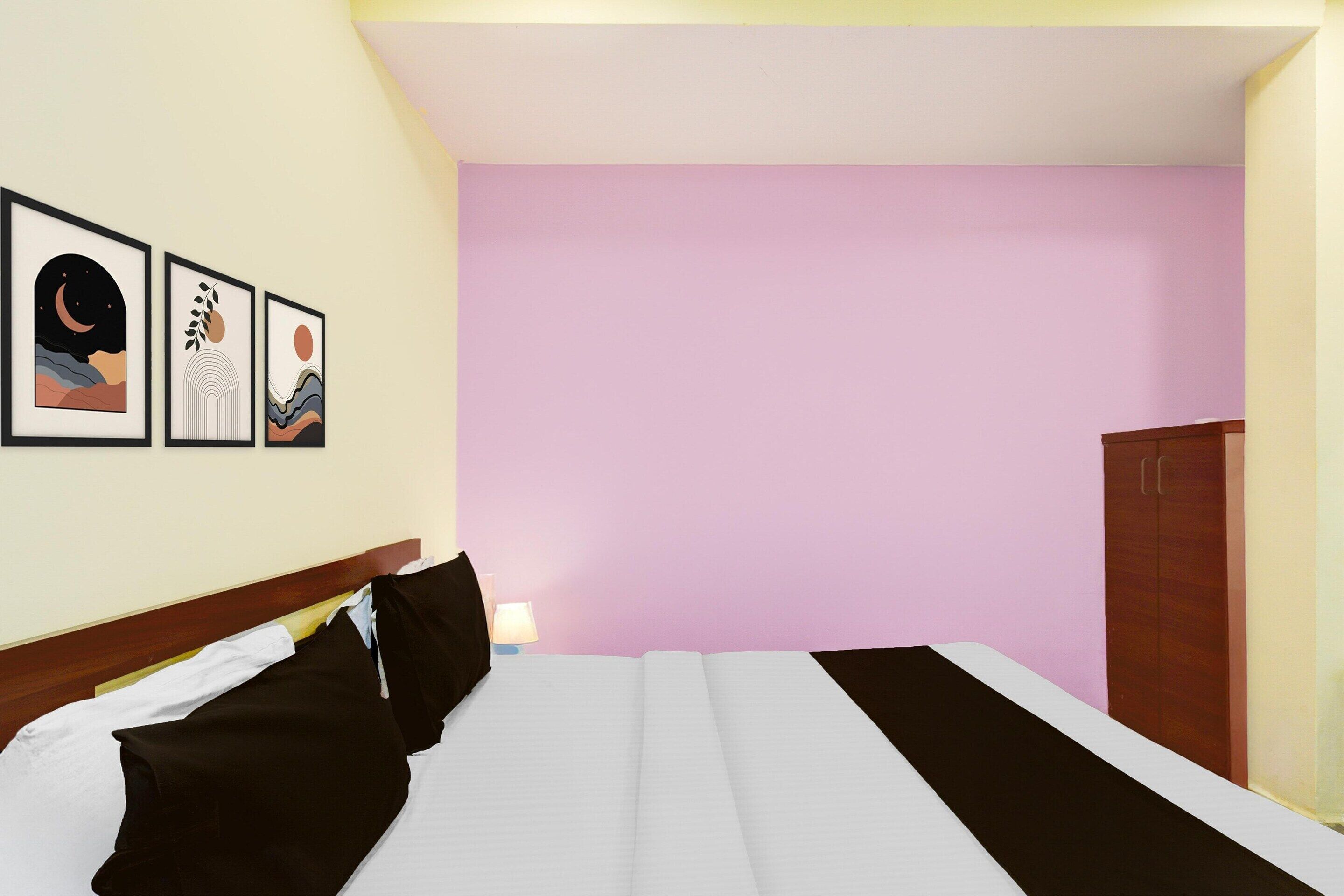 A hotel room with a bed, a nightstand, a lamp, and three framed pictures on the wall.