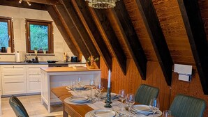 A dining area with a wooden table set for four, a chandelier, and a view of a kitchen with a window.