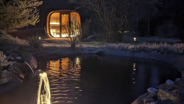 A cabin with a water feature in front, surrounded by trees.