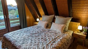 A bedroom with a large bed, wooden beams, a window with a view, and a hanging light fixture.