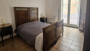 Camera da letto con un letto di legno, un comodino, una lampada, un termosifone e vista all'esterno tramite una porta scorrevole.