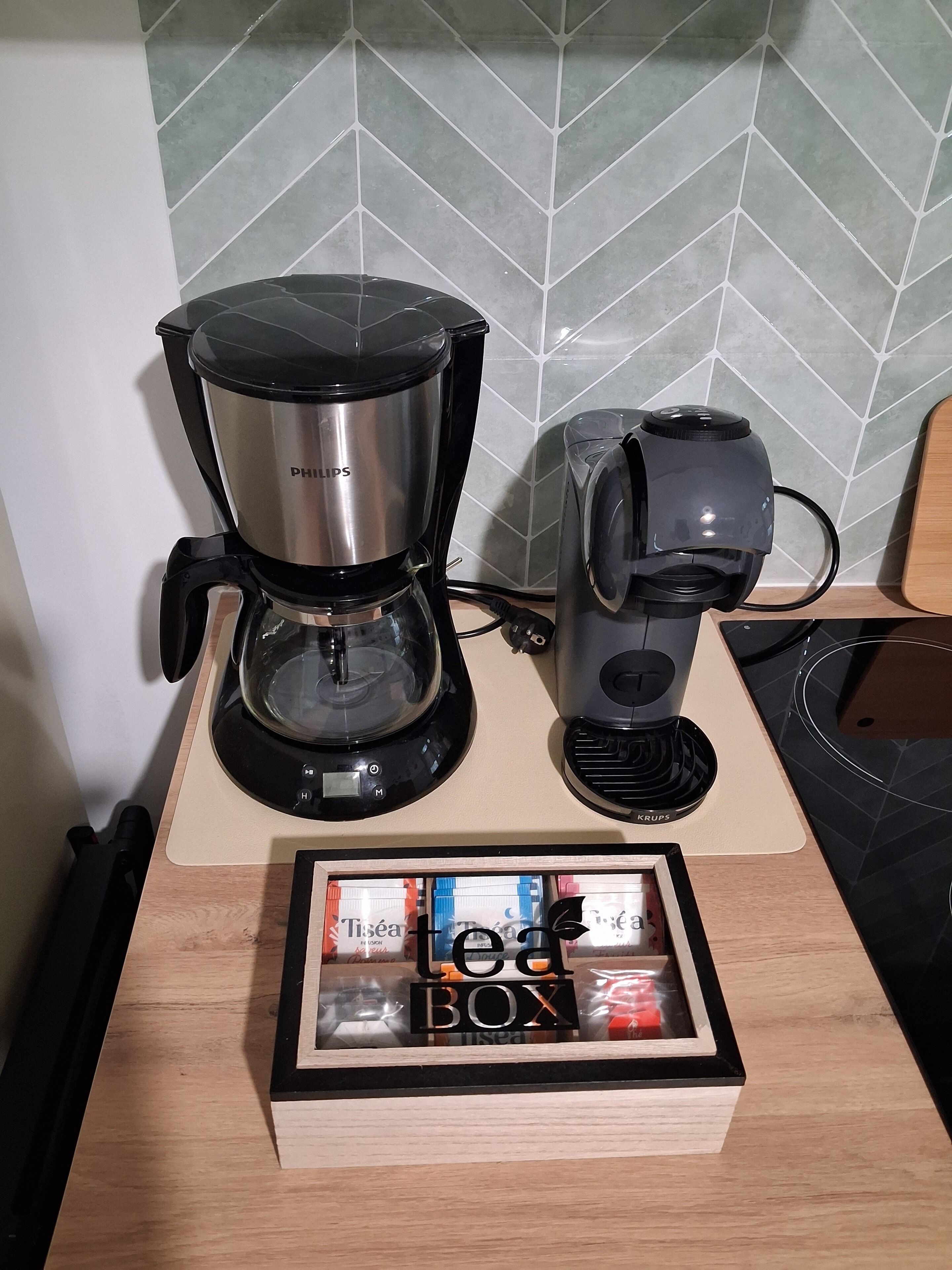 A coffee maker, a kettle, and a box of tea on a kitchen counter.