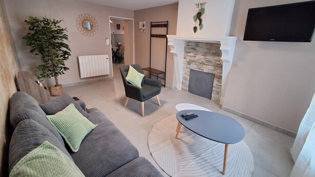 Een woonkamer met een bank, fauteuil, open haard, televisie en een potplant.