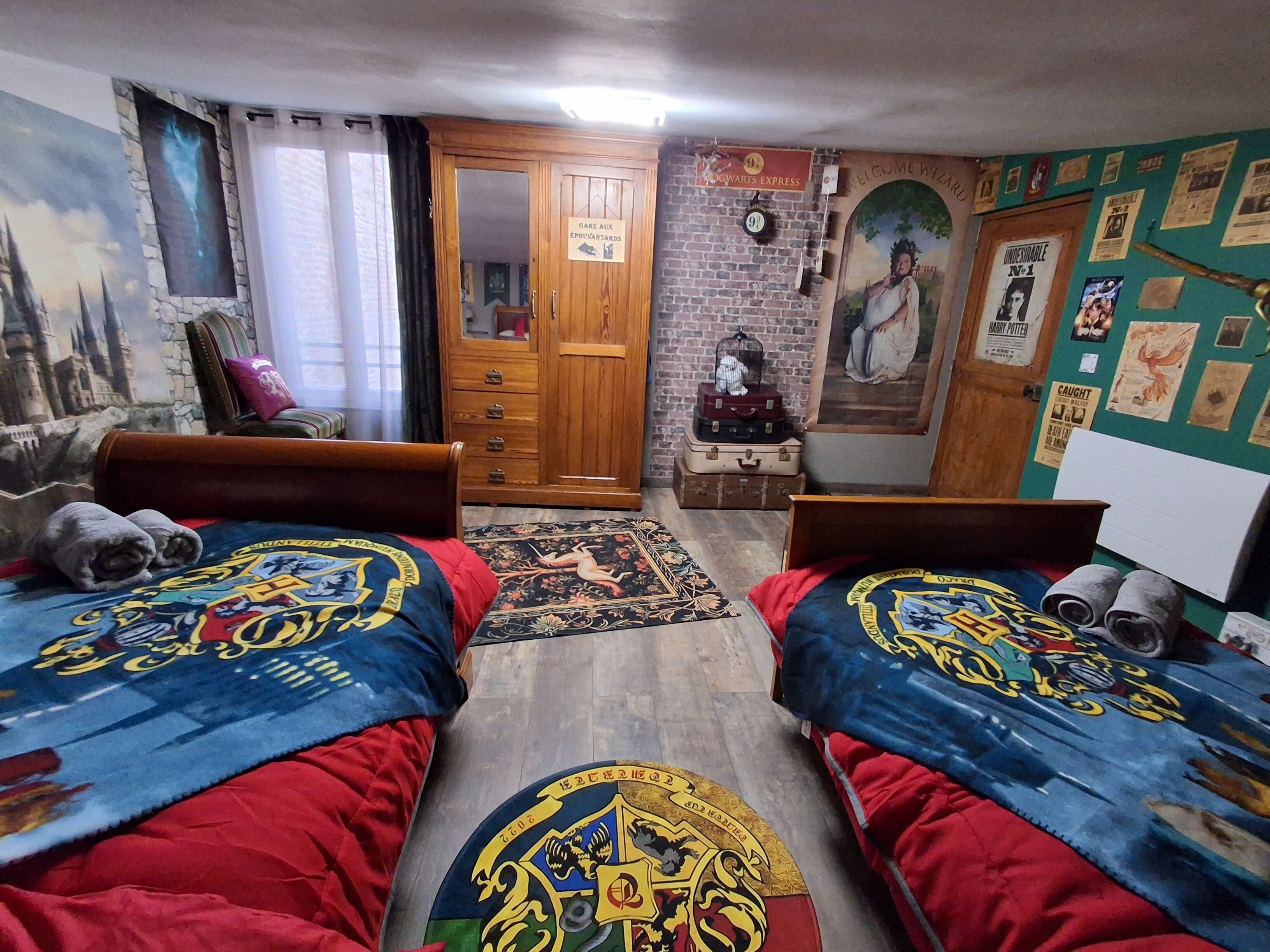 Une chambre avec deux lits, une armoire en bois, une porte avec une pancarte et un mur recouvert d’affiches.