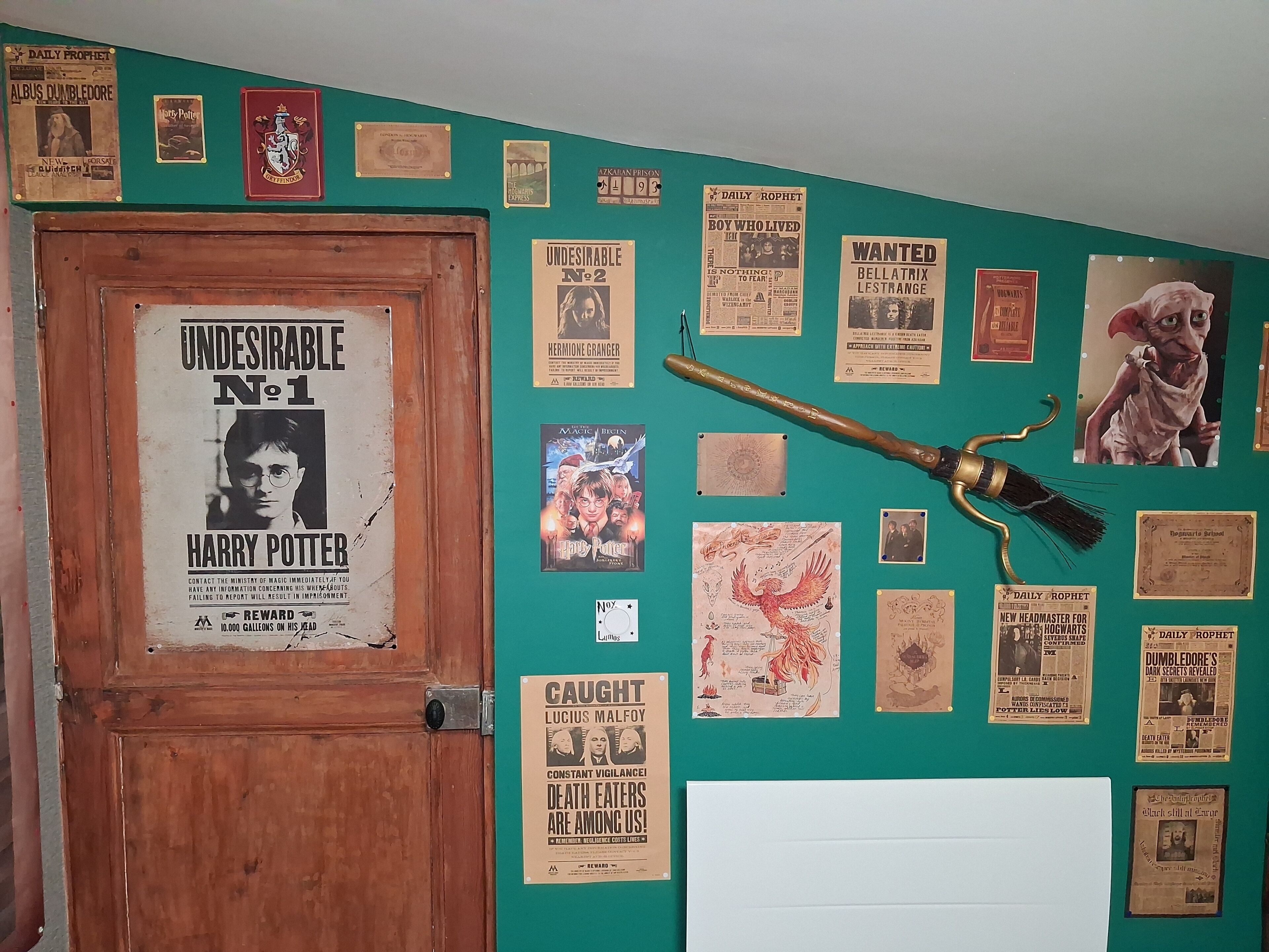 Une pièce dont un mur est peint en vert et orné de divers affiches et objets de collection, notamment une affiche de Harry Potter, une baguette magique et un balai.