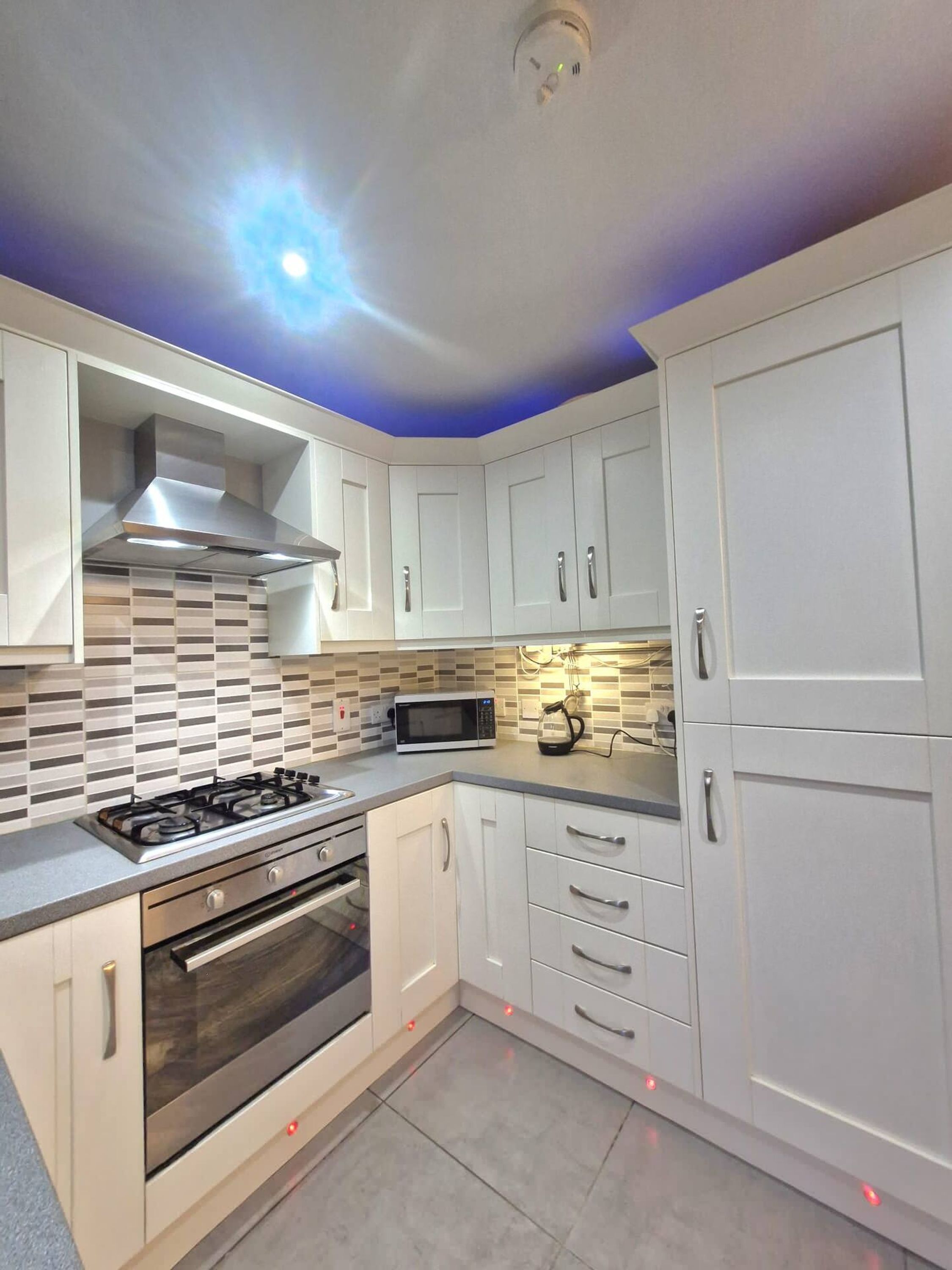 A modern kitchen with white cabinets, a gas stove, a microwave, and a stainless steel range hood.
