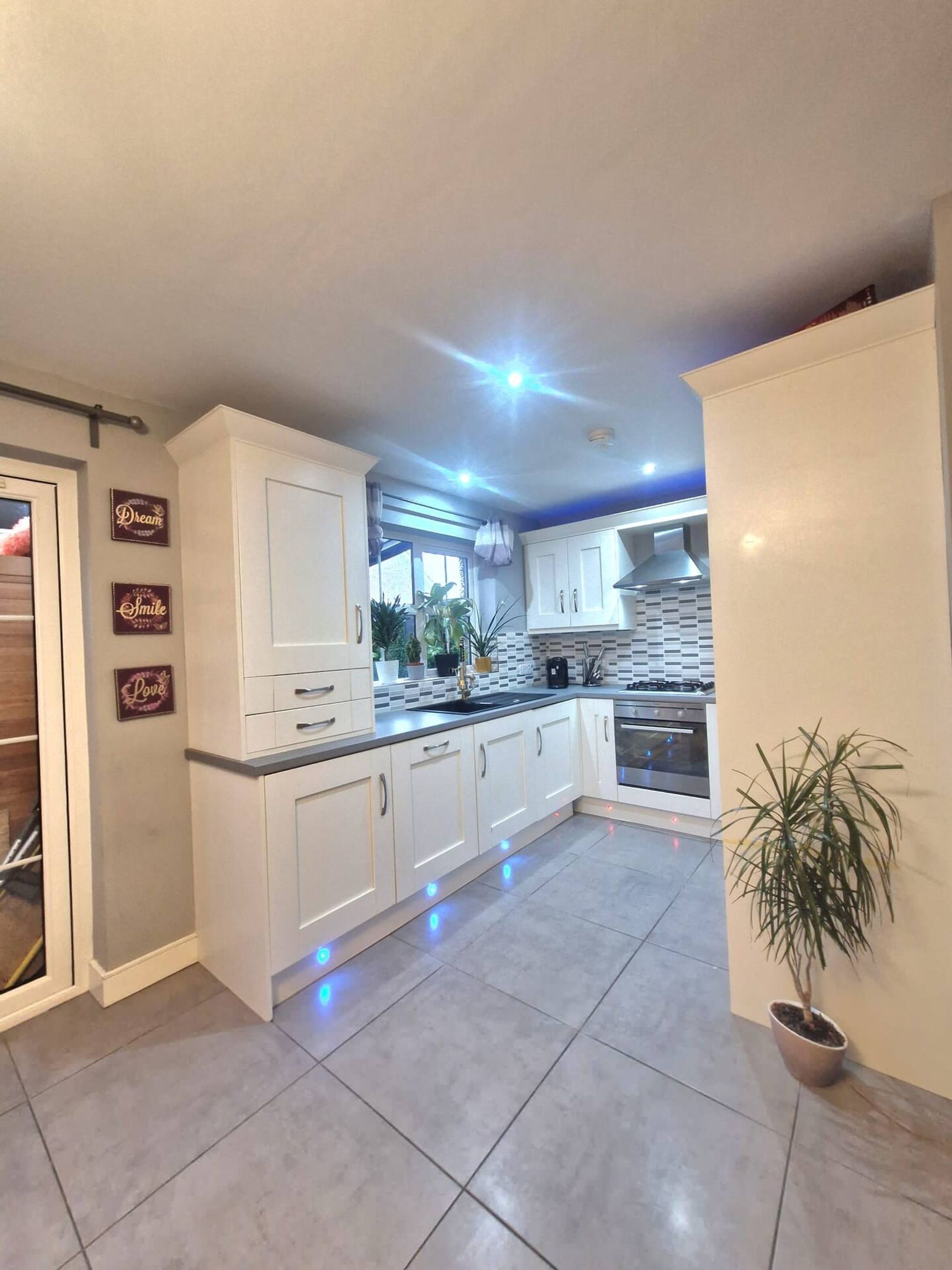 A modern kitchen with white cabinets, a tiled floor, and a potted plant.
