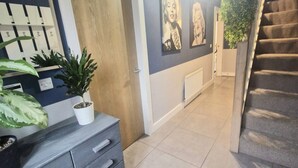 A hallway with a staircase, a wooden door, a radiator, and a potted plant. - 3BR Tropical Escape in Lisburn and Castlereagh (Lisburn)