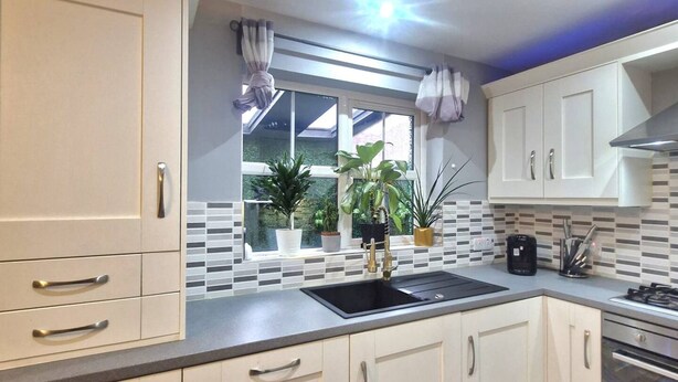 A modern kitchen with white cabinets, a black sink, and a window with plants. - 3BR Tropical Escape in Lisburn and Castlereagh (Lisburn)
