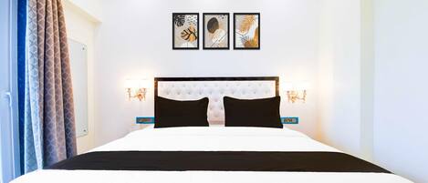 A hotel room with a large bed, a tufted headboard, wall-mounted artwork, and bedside lamps.