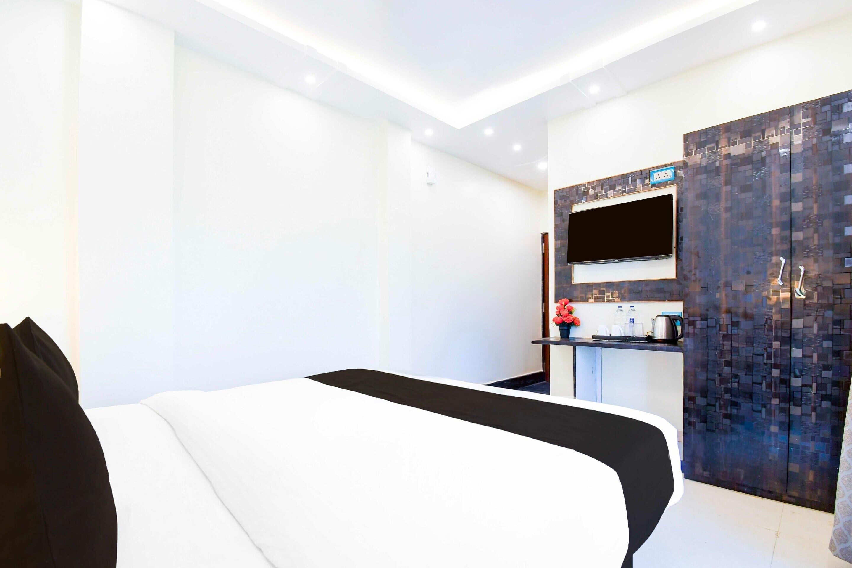 A modern hotel room with a bed, a small kitchenette, and a TV mounted on the wall.