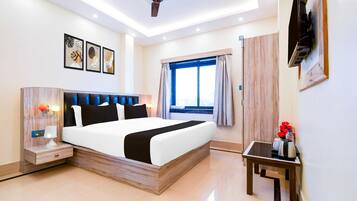A modern hotel room with a bed, bedside table, lamp, artwork, ceiling fan, window, and a small table with a vase.