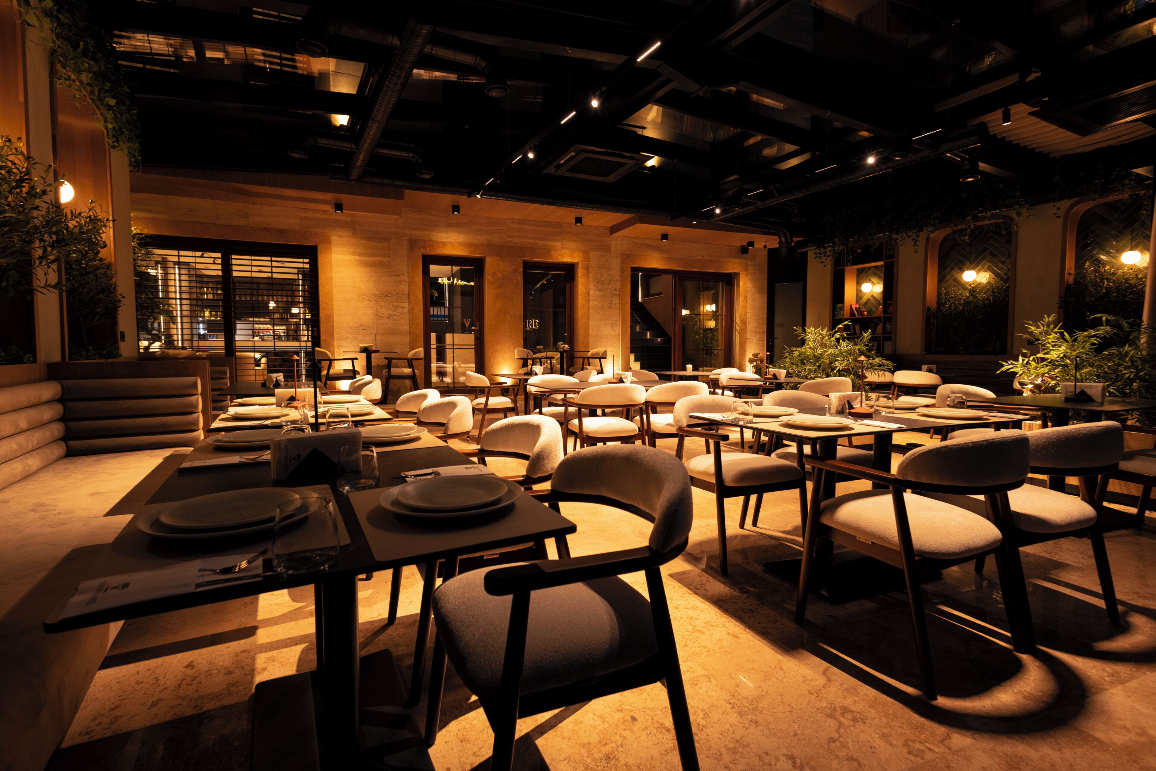 A restaurant with multiple tables and chairs, a bar area, and a view of the cityscape through large windows.