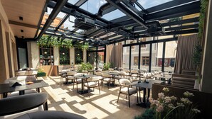 A modern cafe with a glass ceiling, indoor plants, and a view of the street.