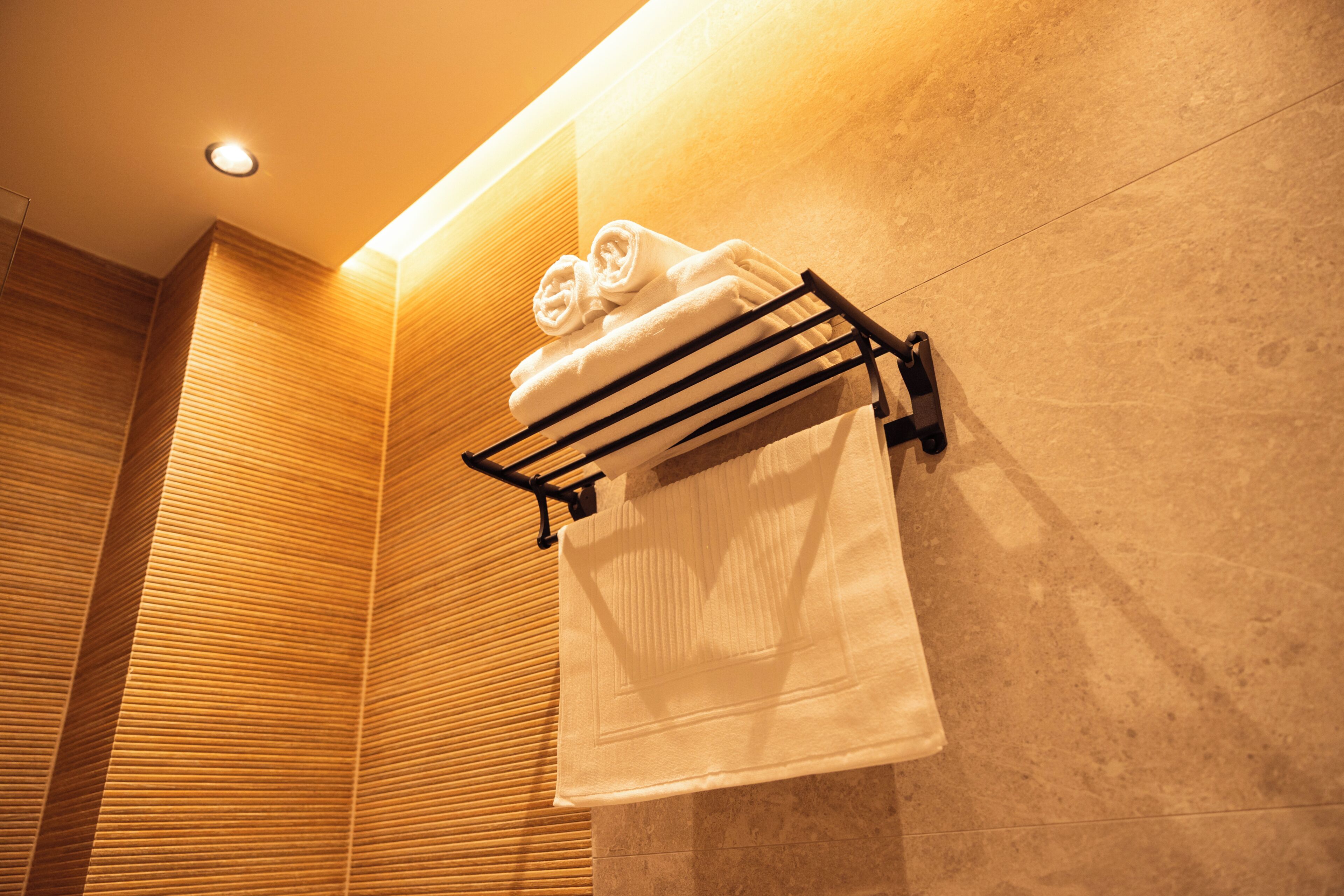A bathroom with a towel rack holding two towels, a wooden wall, and a ceiling light.