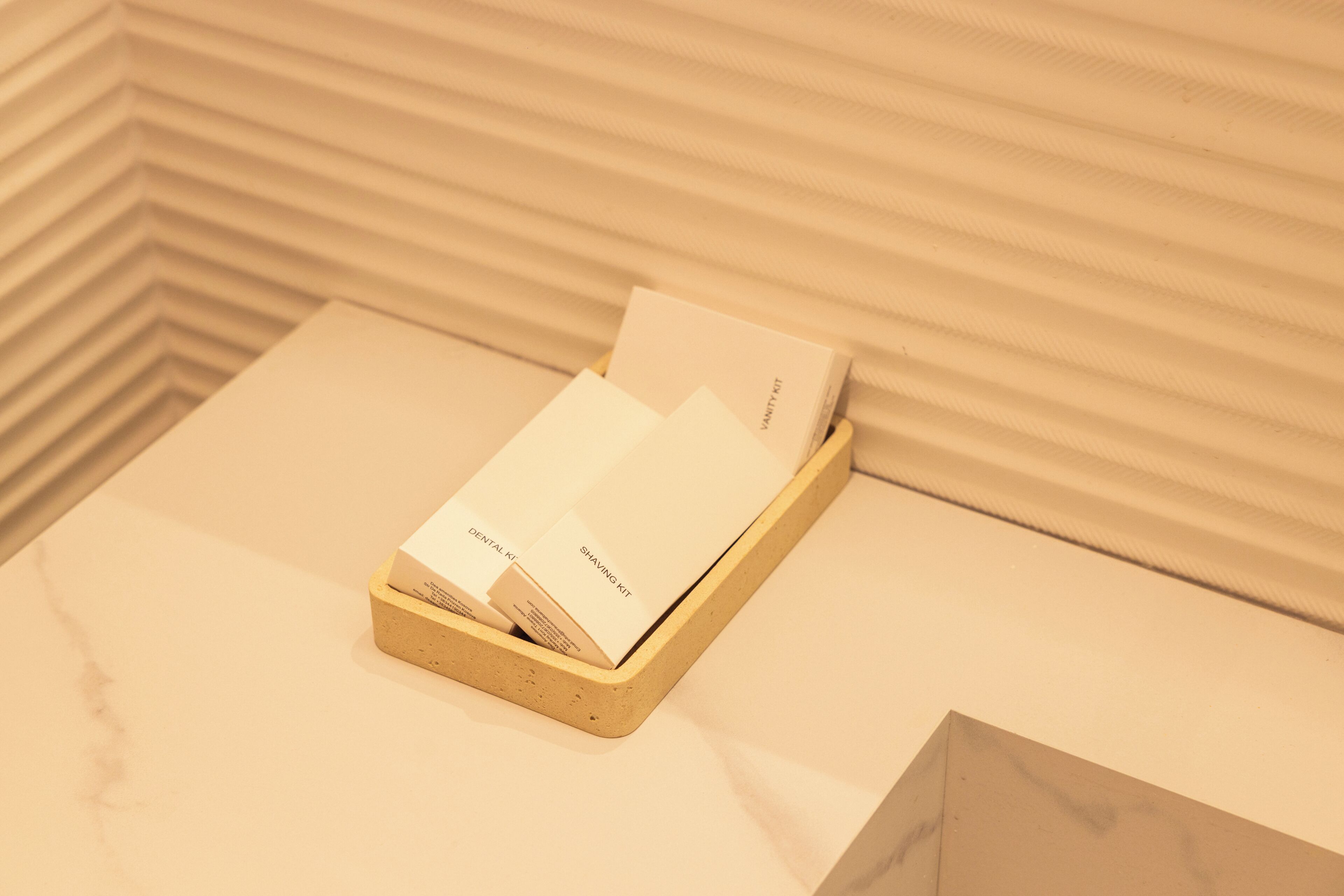 A wooden tray with two white boxes labeled 'Dental Kit' and 'Shaving Kit' on a marble surface.