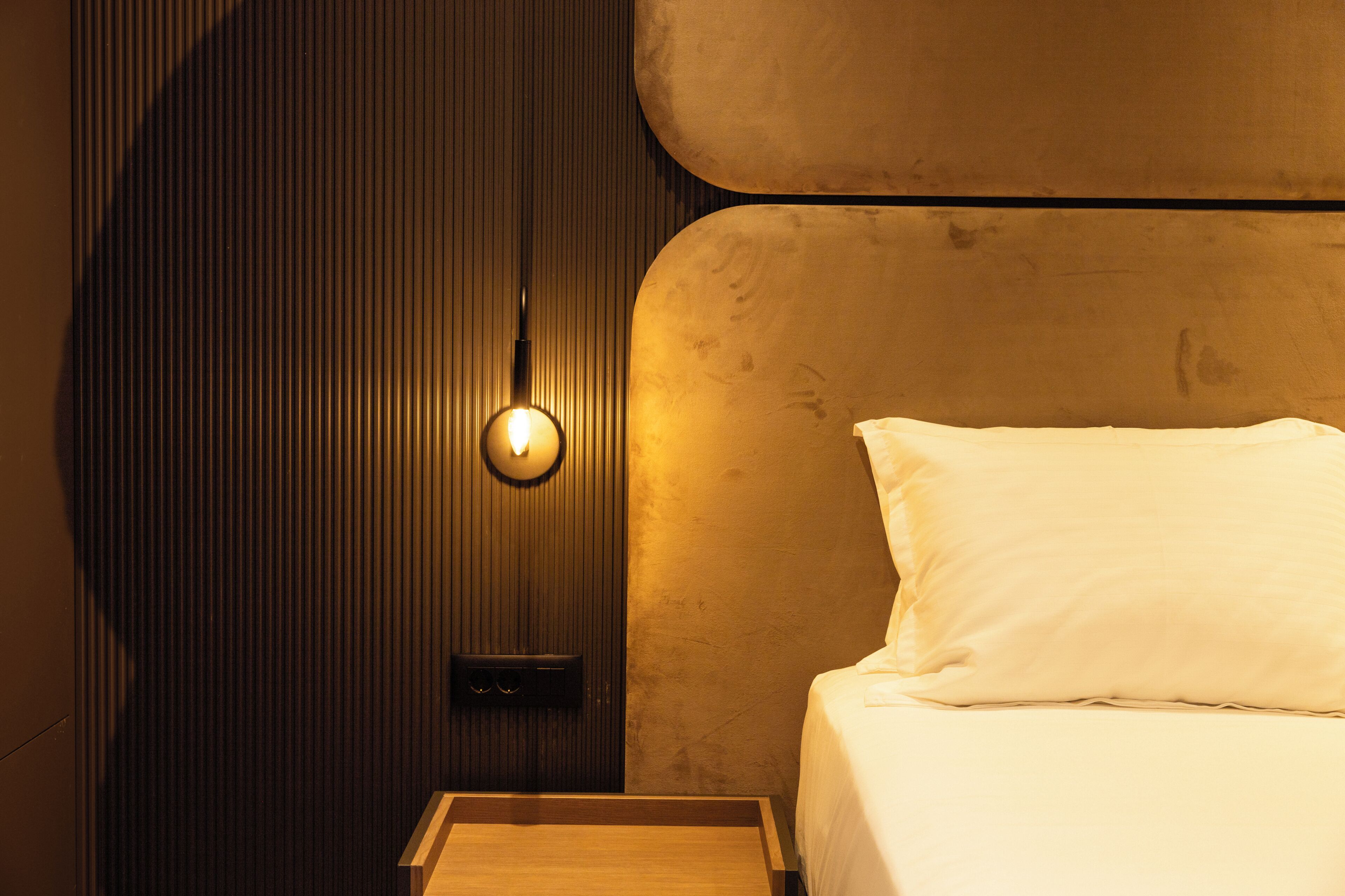 Una habitación de hotel con una cama, una mesita de noche y una lámpara de pared.