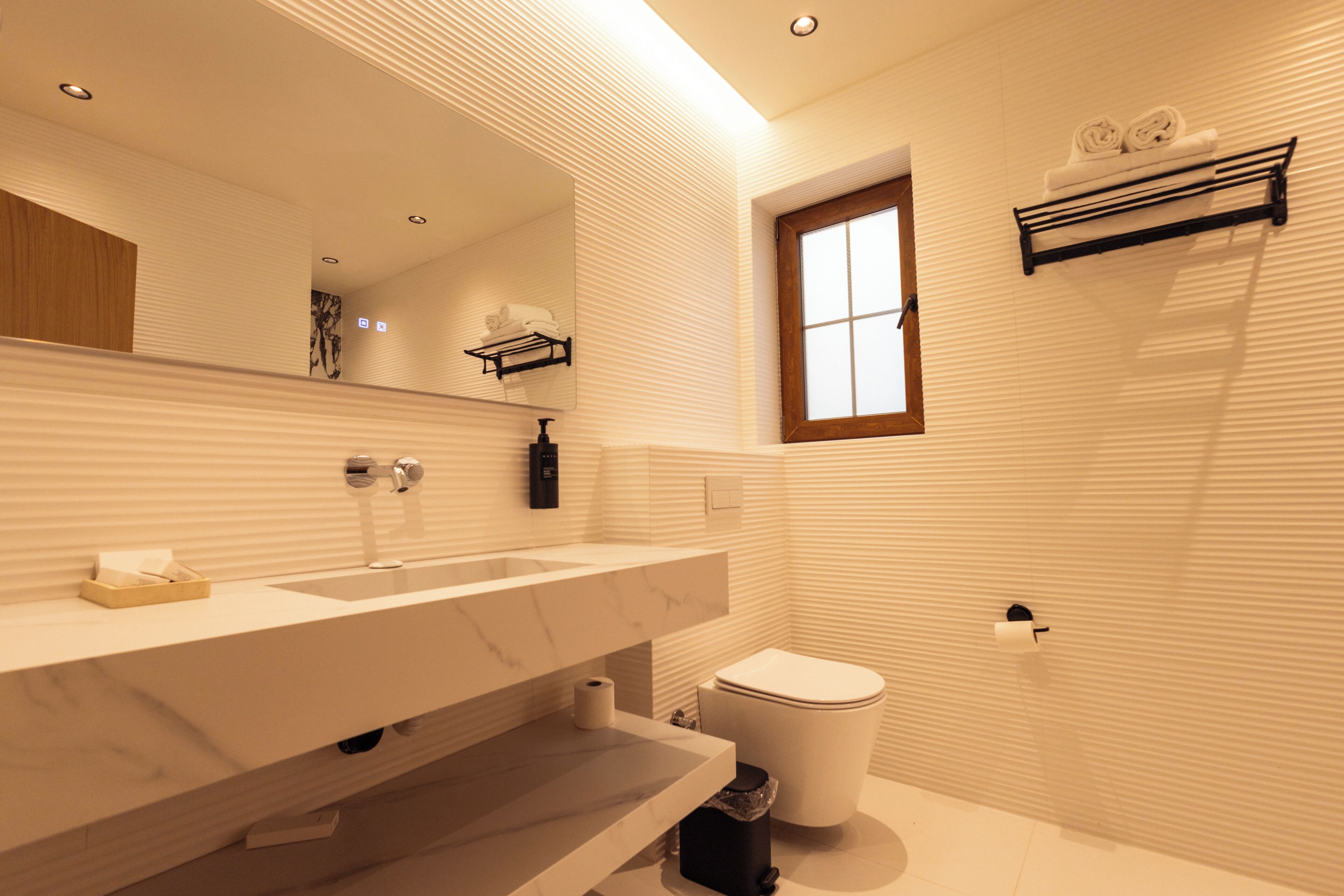 Une salle de bain moderne avec un grand miroir, un lavabo en marbre, des toilettes et une fenêtre.