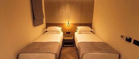 A hotel room with two beds, a nightstand, a wall-mounted light, and a wooden floor.