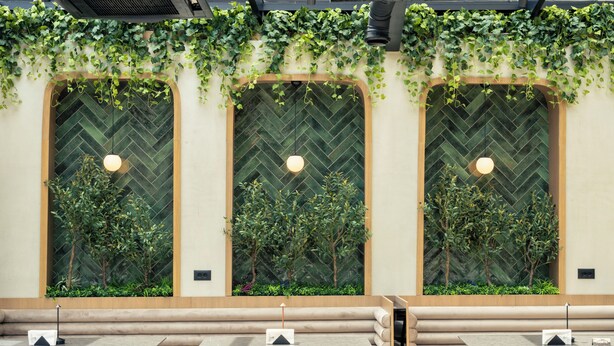 A restaurant with three large windows, each with a herringbone pattern, and a seating area with round tables and cushioned benches.