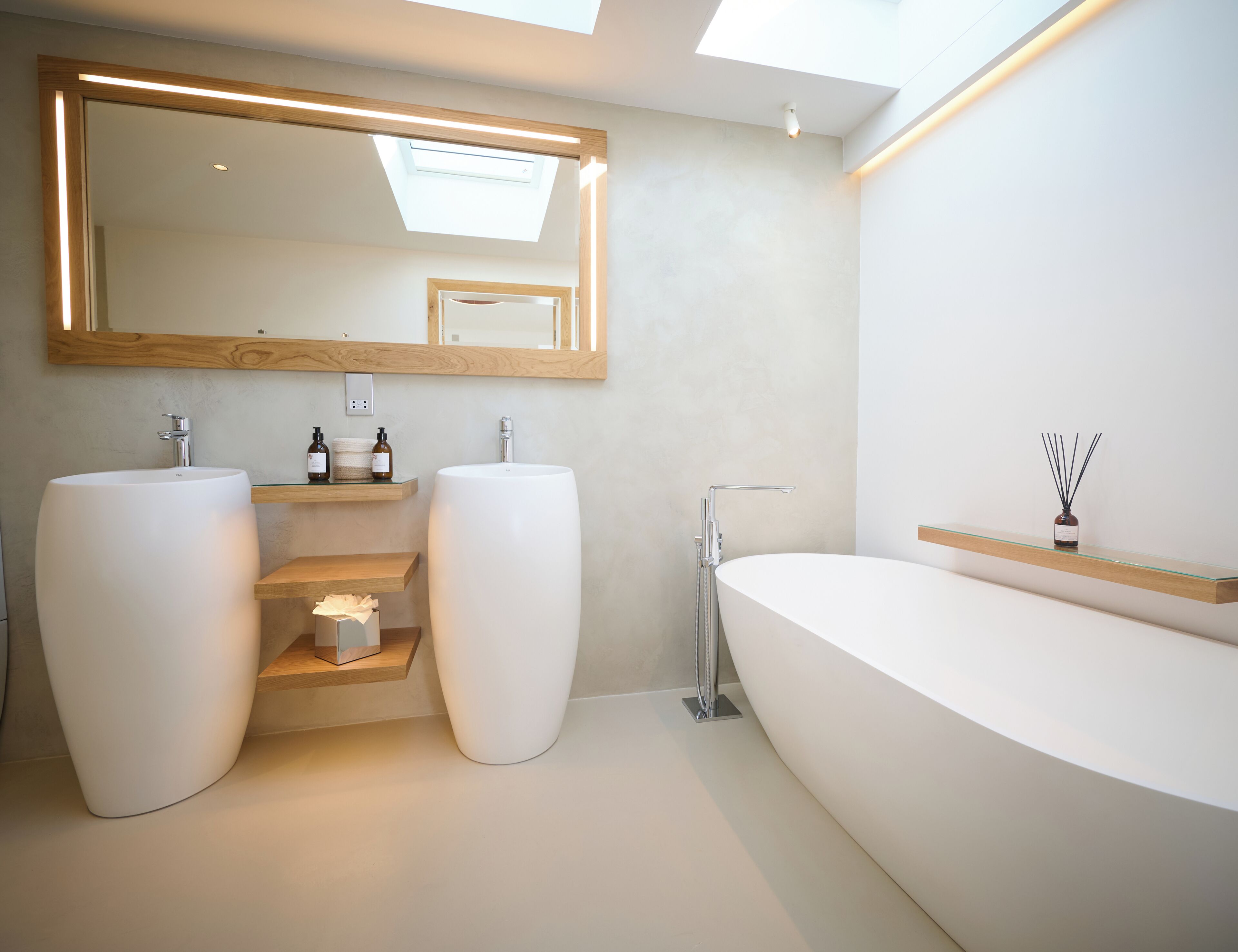 A modern bathroom with two large sinks, a freestanding bathtub, a skylight, and a mirror with a wooden frame.