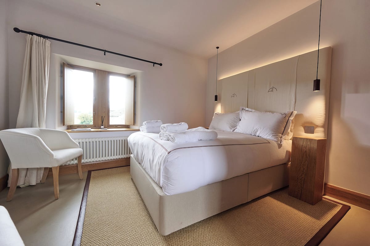 Un dormitorio moderno con cama, mesita de noche, silla y ventana con cortinas.