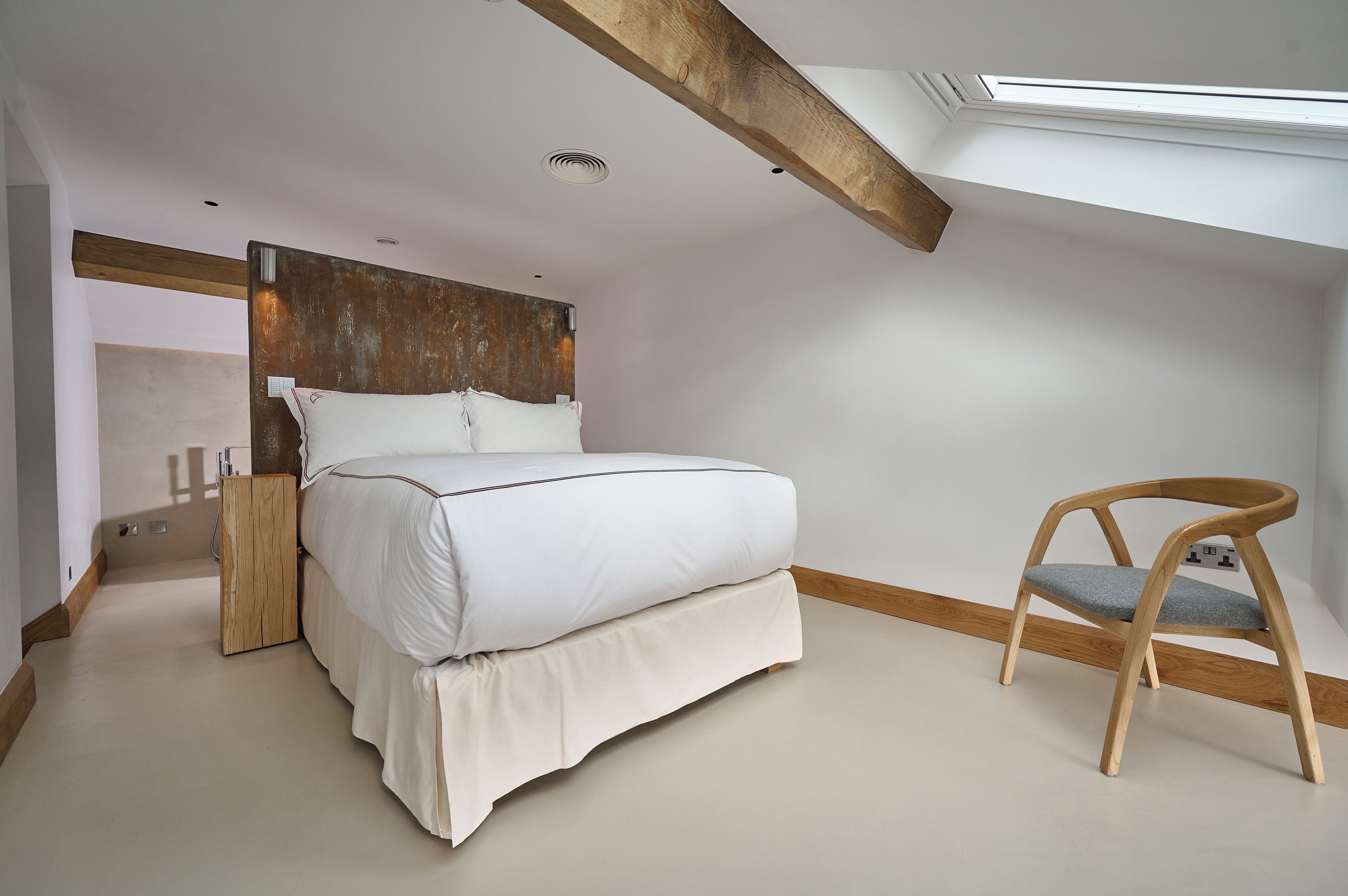 A bedroom with a bed, a wooden chair, a wooden headboard, and a skylight.
