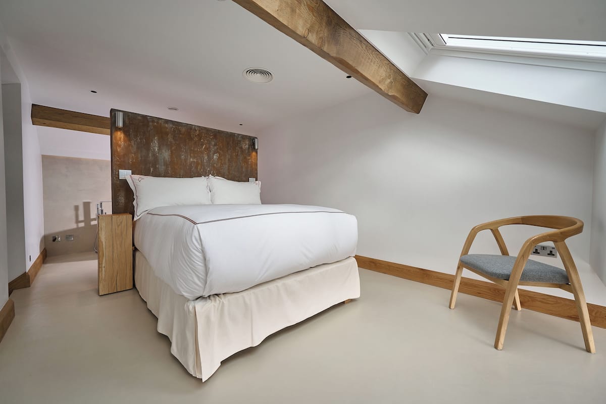 Un dormitorio con una cama, una silla de madera, un cabecero de madera y un tragaluz.