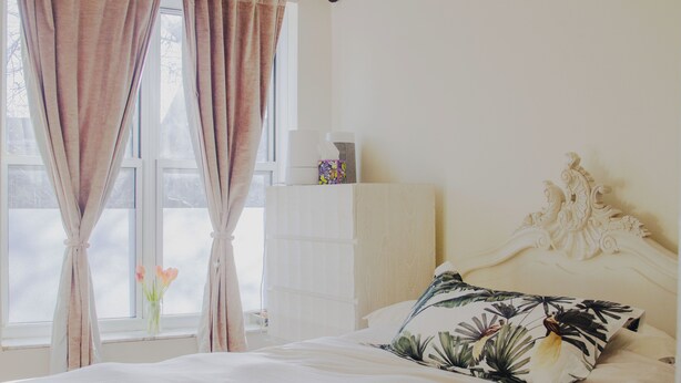 A bedroom with a bed, curtains, a vase with flowers, and a decorative headboard.