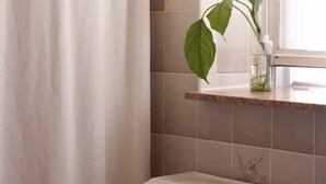 A bathroom with a shower curtain, a toilet, a sink, and a window with a plant.