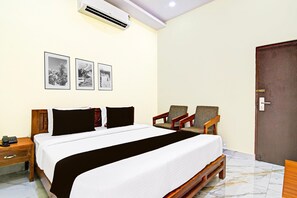 Una habitación de hotel con una cama, dos sillones, una mesita de noche de madera y tres cuadros en la pared.