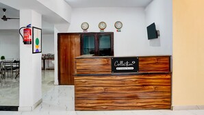 Un mostrador de recepción con detalles de madera, un extintor y tres relojes en la pared.