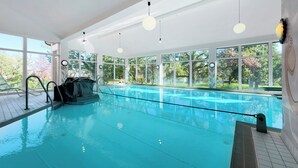 Una amplia piscina interior con paredes de vidrio transparente, un trampolín y un tobogán de agua.