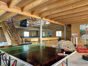Ein Tischtennistisch in einem Raum mit Holzbalken, einer Treppe und einem Wandgemälde.