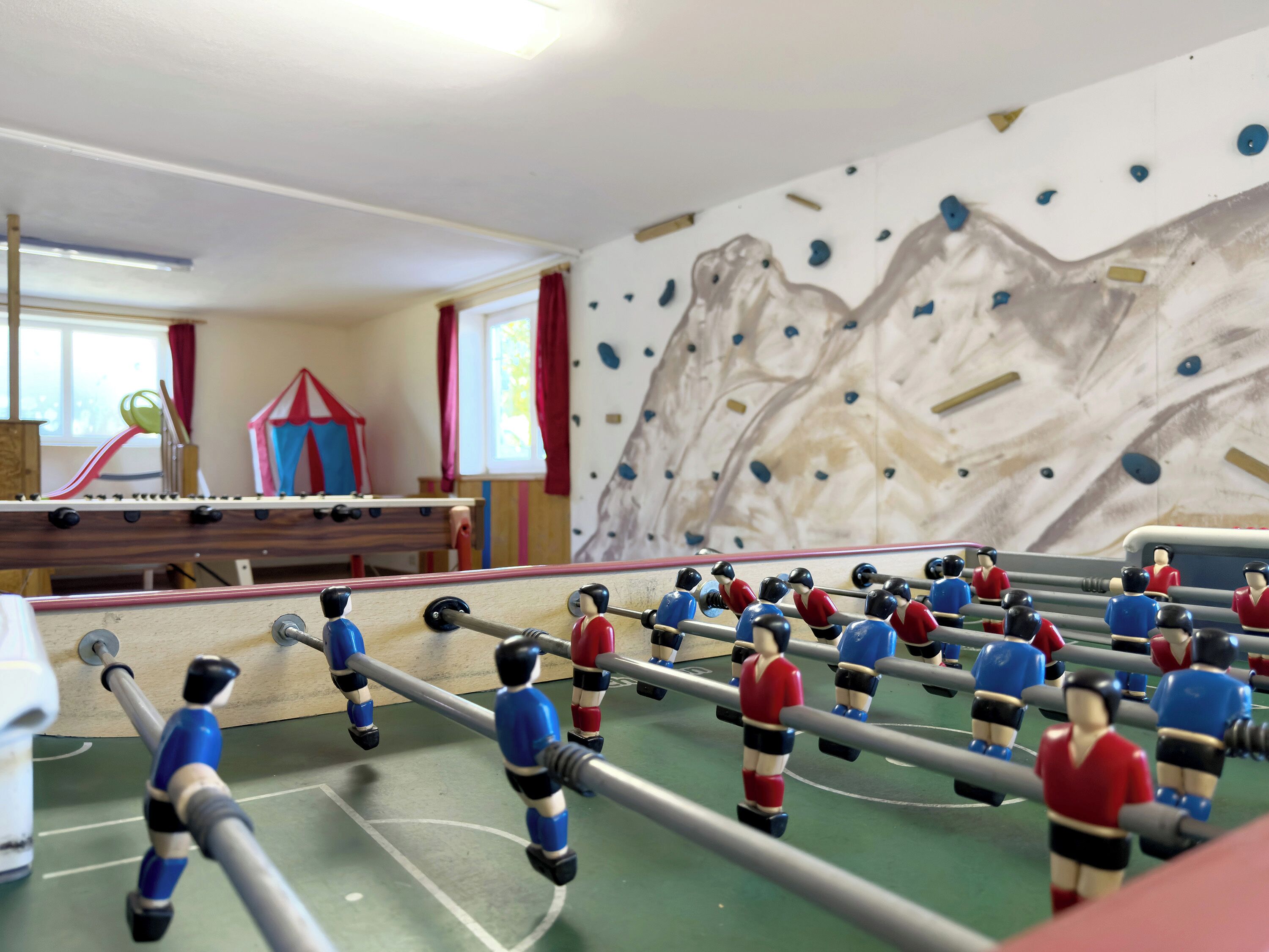 A room with a foosball table, a climbing wall, and a window with curtains.
