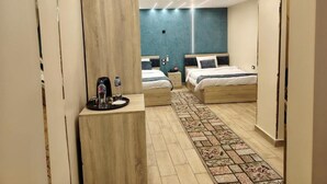 A modern hotel room with two beds, a small desk with a coffee maker, and a patterned rug.