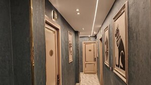 A hallway with doors numbered 13 and 11, marble flooring, and framed artwork on the walls.
