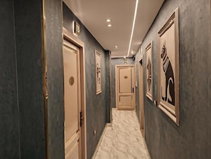 Un couloir avec des portes numérotées 13 et 11, un sol en marbre et des œuvres d’art encadrées accrochées aux murs.