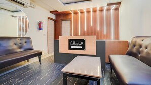 A modern reception area with a wooden reception desk, a black leather sofa, and a small table. - Saver Single Royal Inn (New Delhi)