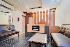 A reception area with a wooden reception desk, a black leather sofa, a small table, and a fire extinguisher on the wall. - Saver Single Royal Inn (New Delhi)