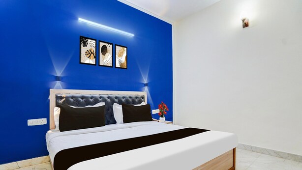 A bedroom with a bed, a nightstand, a wall-mounted light, and three framed pictures. - Saver Single Royal Inn (New Delhi)